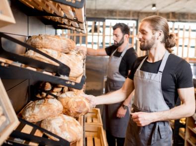 A person in aprons standing next to a shelf with bread
