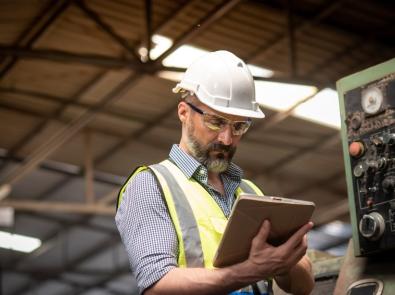 A person wearing a hard hat and safety vest holding a tablet